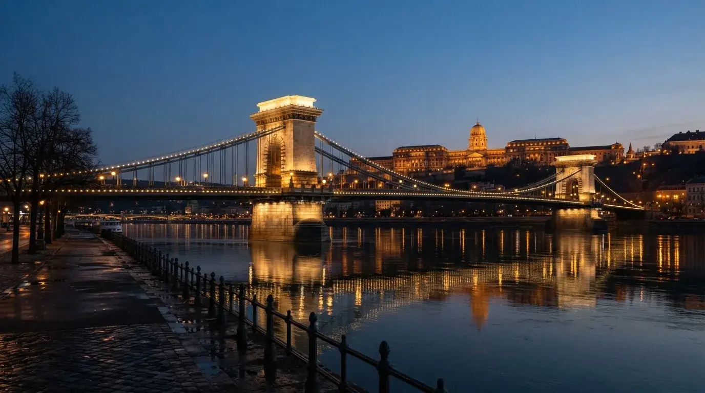 A budapesti Lánchíd esti fényekben a Duna fölött, a háttérben a budai Vár, forgalom nélküli rakpart.